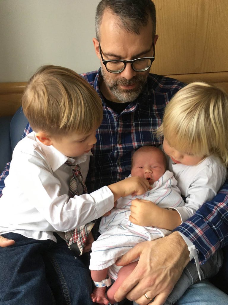 Dad with newborn baby and brothers.